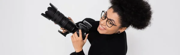 Вид зверху веселий і стильний афроамериканський виробник контенту з цифровою камерою ізольований на сірому, банер — стокове фото
