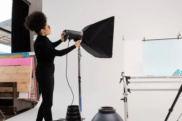 Vista lateral do gerente de conteúdo afro-americano em roupas pretas montando refletor softbox no estúdio de fotos moderno — Fotografia de Stock