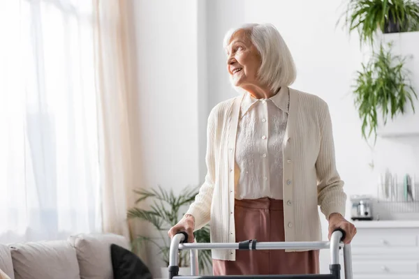 Glückliche Seniorin mit grauen Haaren geht mit Rollator zu Hause spazieren — Stockfoto