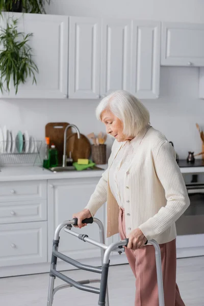 Mujer mayor con el pelo gris caminando con la ayuda de caminar marco en casa - foto de stock