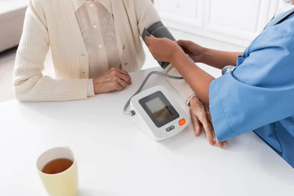 Visão recortada da enfermeira multirracial que mede a pressão arterial da mulher idosa — Fotografia de Stock