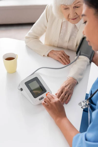 Overhead view of multiracial nurse measuring blood pressure of senior woman with grey hair — Stock Photo
