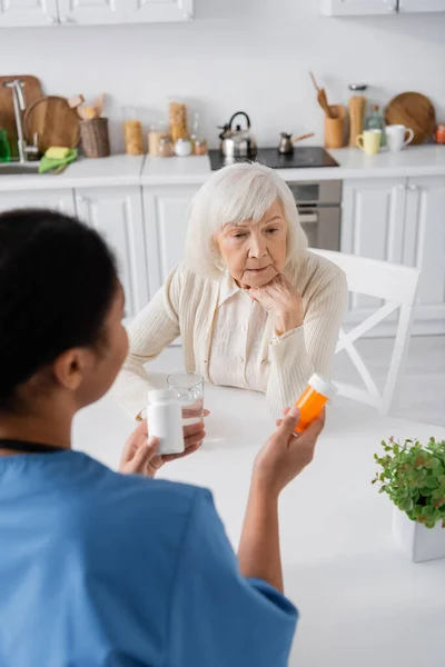 Vista aérea de la enfermera multirracial morena sosteniendo medicación mientras habla con una mujer jubilada con el pelo gris - foto de stock