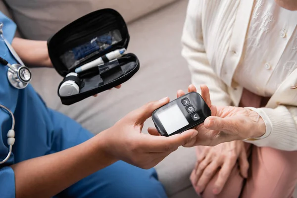 Top view of multiracial nurse holding diabetes kit and giving glucometer to senior woman — Stock Photo
