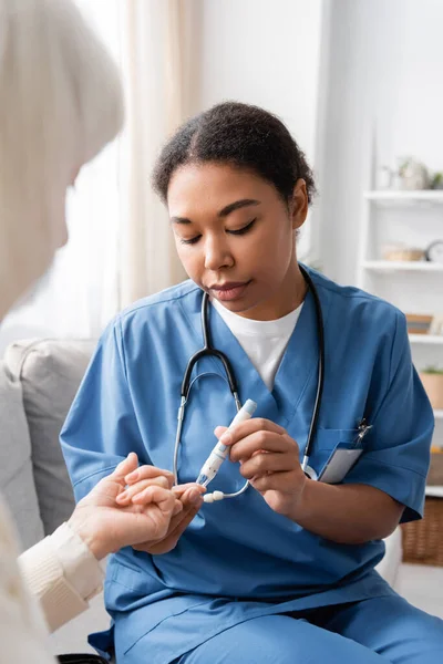 Cuidador multirracial morena tomando amostra de sangue de mulher idosa com caneta lancet — Fotografia de Stock