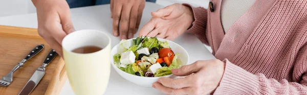 Ausgeschnittene Ansicht eines multirassischen Sozialarbeiters, der in der Nähe einer Seniorin Mittagessen serviert, Banner — Stockfoto