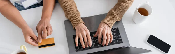 Vista superior de la mujer mayor escribiendo en el teclado del ordenador portátil cerca de trabajador social multirracial con tarjeta de crédito, pancarta - foto de stock