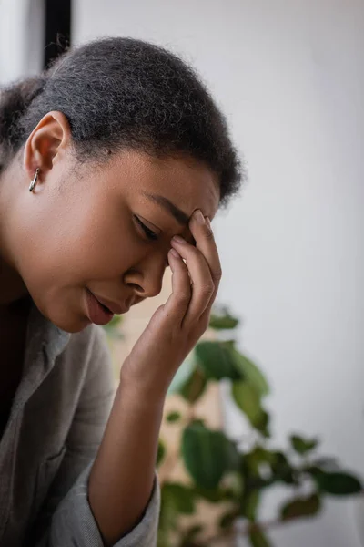 Deprimida mujer multirracial llorando y tocando la frente en casa - foto de stock