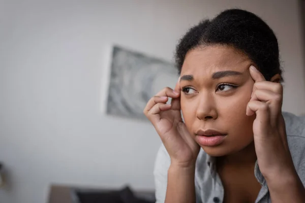 Triste femme multiraciale avec dépression touchant la tête à la maison — Photo de stock