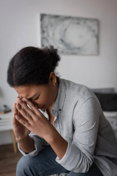 Crying multiracial woman with depression sitting on blurred bed at home — Stock Photo