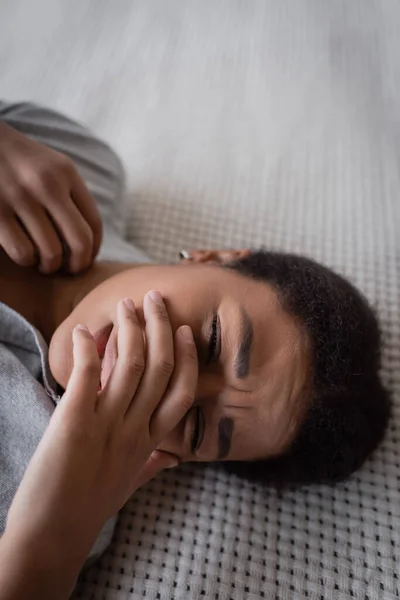 Mujer joven multirracial con problemas psicológicos tumbada en la cama en casa - foto de stock