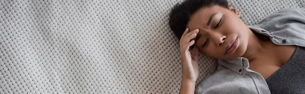Top view of depressed multiracial woman closing eyes while lying on bed, banner — Stock Photo