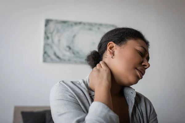 Молодая многонациональная женщина трогает болезненную шею дома — стоковое фото