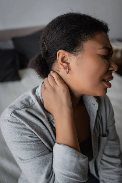 Vista laterale della donna multirazziale che soffre di dolore al collo a letto a casa — Foto stock