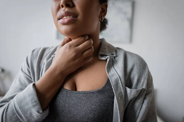 Cropped view of young multiracial woman touching sore throat at home — Stock Photo