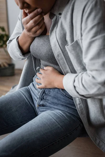 Ausgeschnittene Ansicht einer verschwommenen multirassischen Frau, die zu Hause unter Bauchschmerzen leidet — Stockfoto