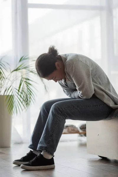 Traurige multirassische Frau fühlt sich unwohl, während sie zu Hause auf dem Bett sitzt — Stockfoto
