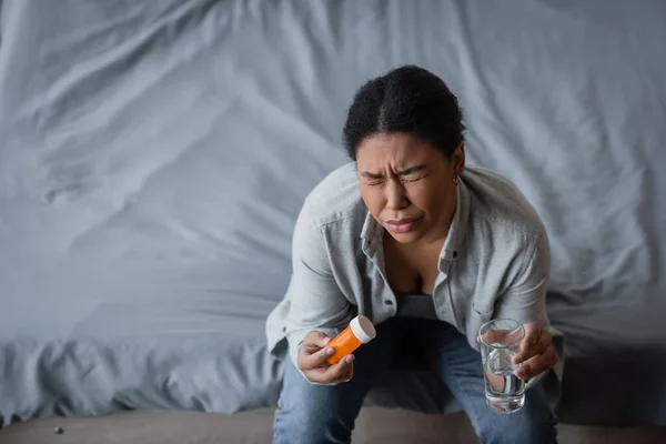 Blick aus der Vogelperspektive auf eine Frau mit Depressionen, die zu Hause Tabletten und Wasser im Bett hält — Stockfoto