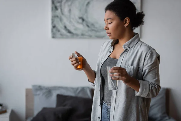 Young multiracial woman holding antidepressant pills and water in bedroom — Stock Photo