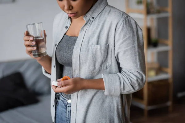Cropped view of multiracial woman holding antidepressant pills and water at home — Stock Photo