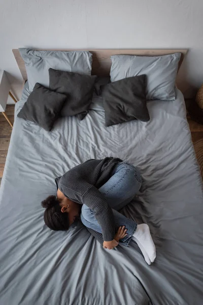Vista superior de la mujer multirracial con depresión acostada en la cama en casa - foto de stock