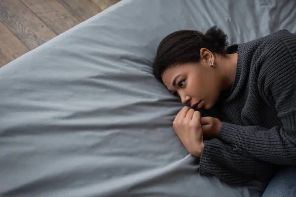 Draufsicht einer multiethnischen Frau mit Depressionen, die wegschaut, während sie im Bett liegt — Stockfoto
