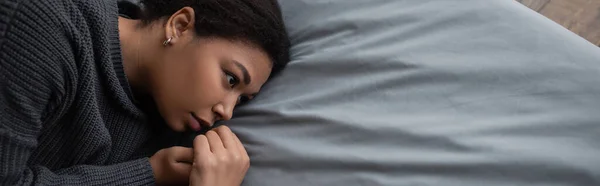 Draufsicht einer depressiven, multiethnischen Frau mit Apathie, die auf dem Bett wegschaut, Banner — Stockfoto