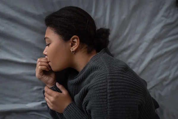Top view of upset multiracial woman with depression lying on grey bedding — Stock Photo