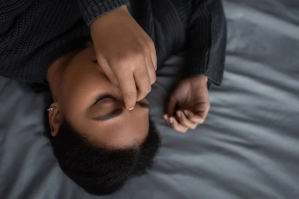 Ansicht von oben: Frustrierte multirassische Frau berührt Gesicht, während sie im Bett liegt — Stockfoto