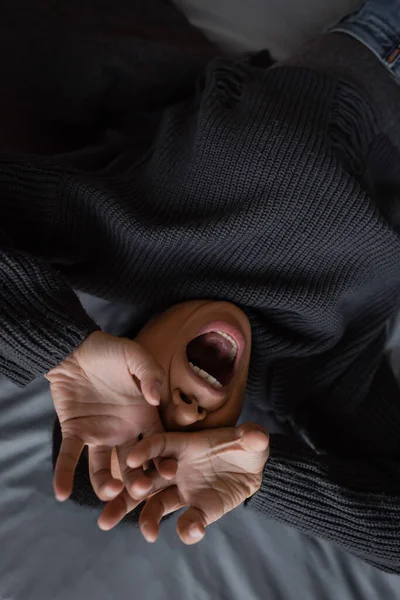 Vista dall'alto della donna stressata multirazziale che copre il viso e urla sul letto a casa — Foto stock