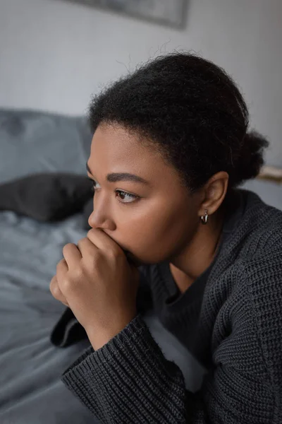 Depressed multiracial woman in sweater lying on bed at home — Stock Photo
