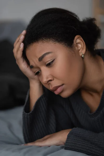 Portrait of upset multiracial woman lying on blurred bed at home — Stock Photo