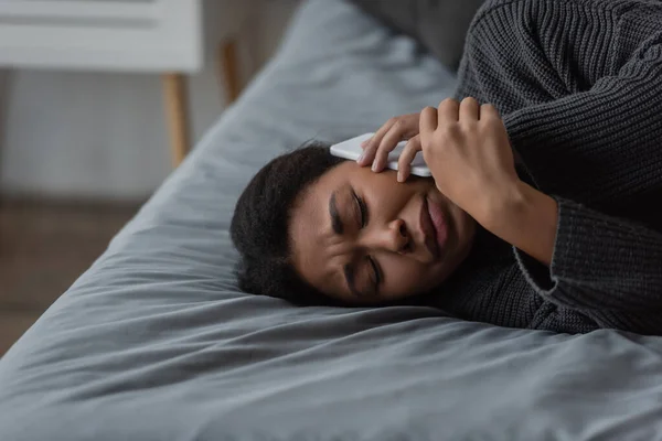 Depresso donna multirazziale chiamando helpline mentre sdraiato sul letto a casa — Foto stock