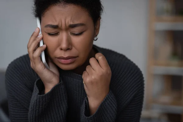 Плачущая многорасовая женщина разговаривает по смартфону с телефоном доверия дома — стоковое фото