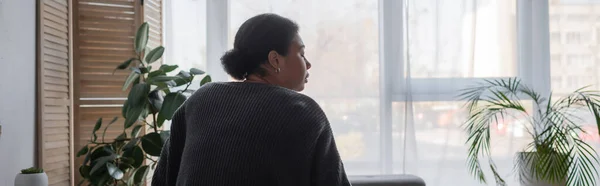 Вид сбоку разочарованной многорасовой женщины в свитере, отводящей взгляд на дом, баннер — стоковое фото