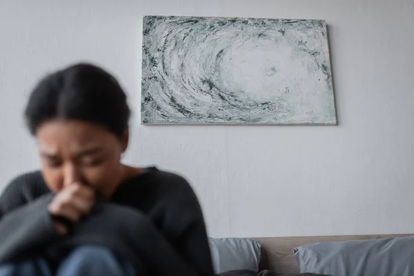 Pintura en la pared cerca de la mujer borrosa multirracial con depresión en el dormitorio - foto de stock