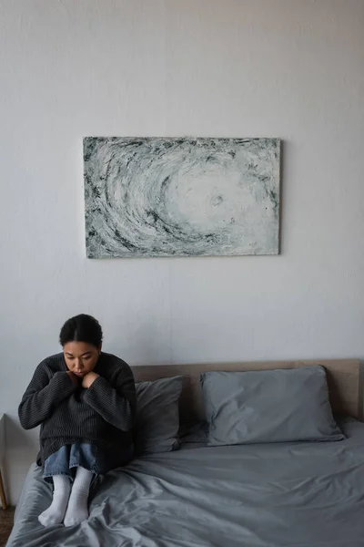 Молодая многонациональная женщина с депрессией сидит на кровати дома — стоковое фото