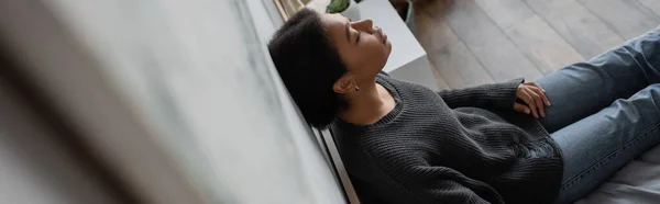 Visão de alto ângulo de mulher multirracial deprimida apoiada na parede enquanto sentada na cama em casa, banner — Fotografia de Stock