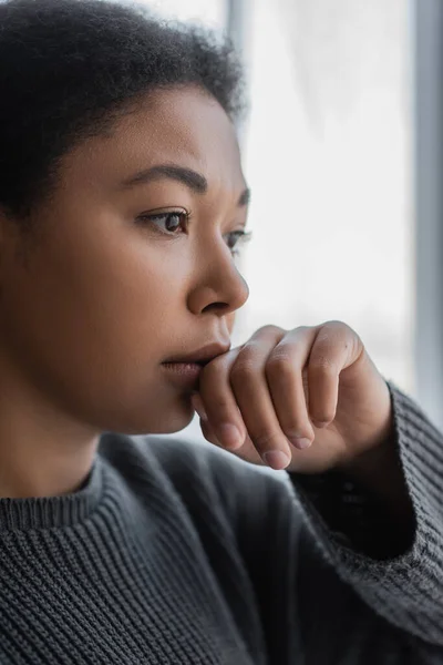 Femme multiraciale frustrée en pull tricoté regardant loin à la maison — Photo de stock