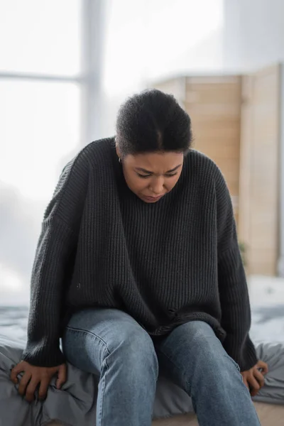 Jeune femme multiraciale avec un problème mental assis sur le lit à la maison — Photo de stock