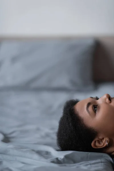 Ausgeschnittene Ansicht einer multirassischen Frau mit Apathie, die aufblickt, während sie zu Hause auf dem Bett liegt — Stockfoto