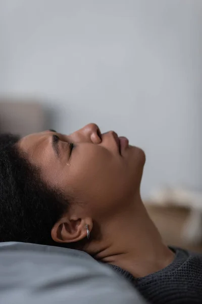 Seitenansicht einer herzzerreißenden multirassischen Frau, die zu Hause auf Kissen weint — Stockfoto