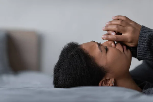 Young multiracial woman with depression crying while lying on bed in bedroom — Stock Photo