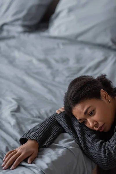 Mujer joven multirracial con apatía sentada cerca de la cama en casa - foto de stock