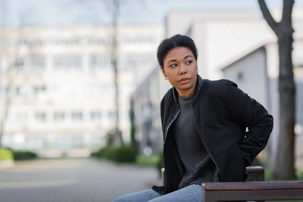 Multiracial woman with apathy looking away while sitting on bench on urban street — Stock Photo