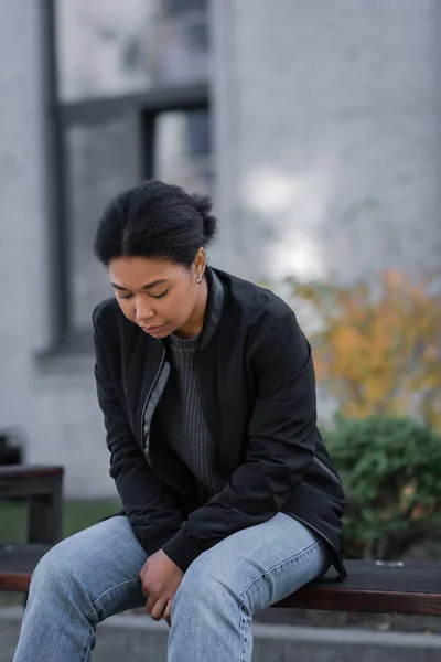 Traurige multirassische Frau mit psychischen Problemen sitzt auf Bank in der städtischen Straße — Stockfoto