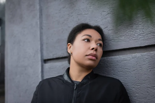 Unzufriedene multirassische Frau mit psychischen Problemen steht in der Nähe einer Mauer im Freien — Stockfoto