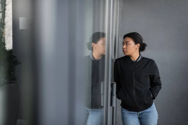 Multiracial woman with depression looking at glass on door of building outdoors — Stock Photo