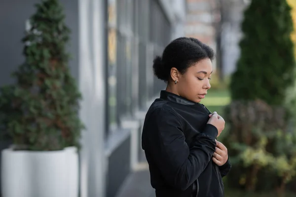Femme multiraciale bouleversée avec un problème psychologique portant une veste sur la rue urbaine floue — Photo de stock