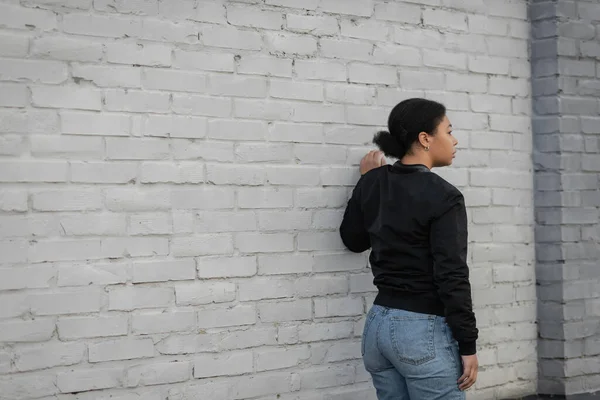 Side view of depressed multiracial woman standing near brick wall on urban street — Stock Photo